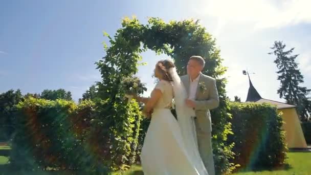 Gli sposi ballano vicino ad un arco verde. La sposa gira intorno allo sposo. Danza nuziale degli sposi. - Filmati, video