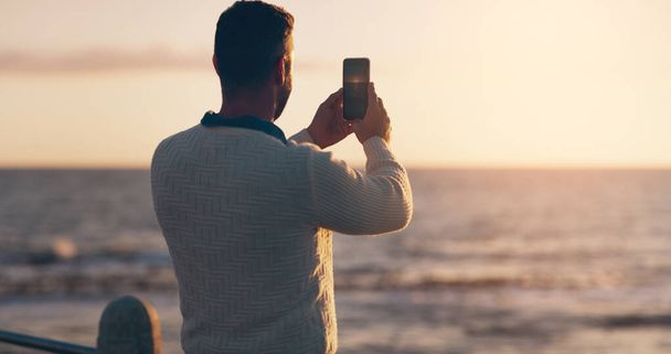 Lefényképezem a gyönyörű naplementét. Visszapillantás egy férfiról, aki a parton napnyugtát fotózza. - Fotó, kép
