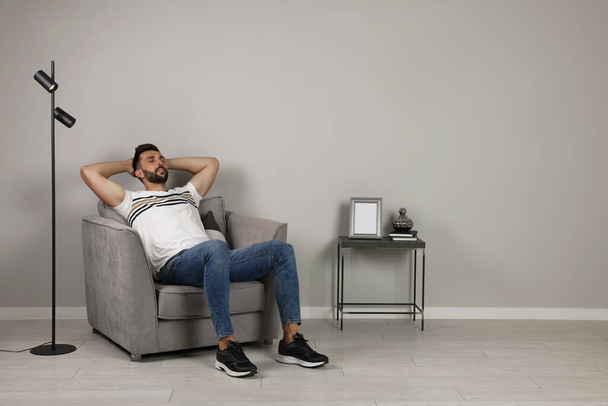 Man napping in armchair near gray wall, space for text - Фото, изображение