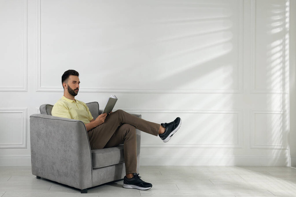 Man reading book in armchair near white wall, space for text - Photo, Image