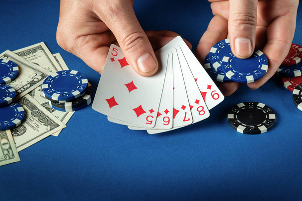 プレーヤーは、クラブでチップやお金と青いテーブルの上にポーカーゲームでストレートフラッシュ勝利の組み合わせでトランプを置きます - 写真・画像