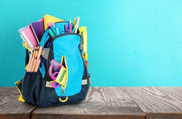 Backpack with school stationery on wooden table against light blue surface, space for text - Fotoğraf, Görsel