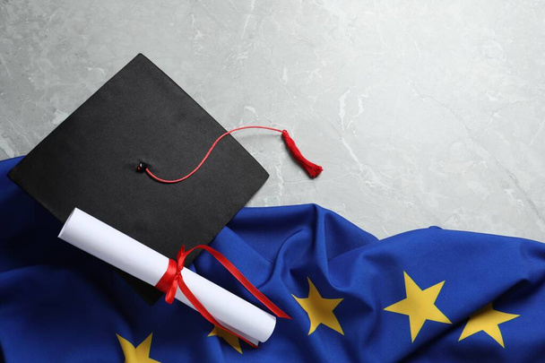 Black graduation cap, diploma and flag of European Union on light grey marble table, flat lay. Space for text - Foto, afbeelding