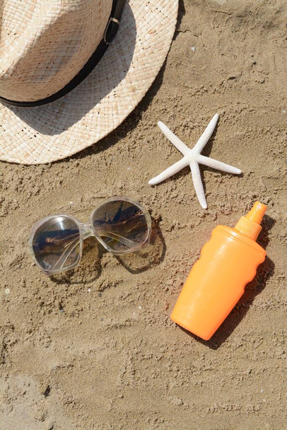 Blank bottle of sunscreen, starfish and beach accessories on sand, flat lay - Photo, image