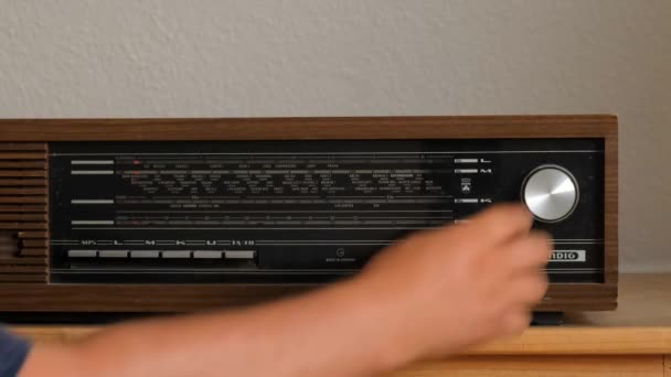 Ένα παλιό ξύλινο ραδιόφωνο GRUNDIG. Το χέρι ενός άντρα στριφογυρίζει το κουμπί της μελωδίας στο ράδιο κύμα. - Πλάνα, βίντεο
