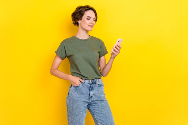 Portrait of nice positive woman bob hairdo dressed khaki t-shirt hand in pocket read social media isolated on yellow color background. - Foto, Imagen