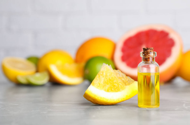 Bottle of essential oil with different citrus fruits on grey marble table. Space for text - Fotografie, Obrázek