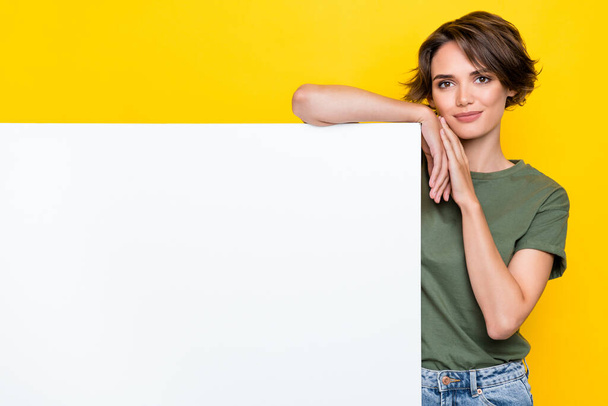 Portrait of pretty gorgeous cute girl bob hairstyle wear khaki t-shirt hold hand on white banner isolated on yellow color background. - Foto, afbeelding