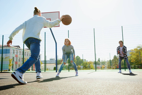 Group of teens, students playing street basketball at basketball court outdoors at spring sunny day. Sport, leisure activities, hobbies, team, friendship. Boys and girl spending time together. - Foto, immagini