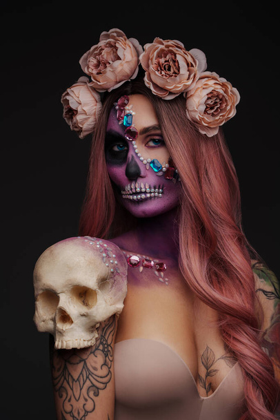 Studio shot of spooky female model with makeup and skull head against dark background. - Foto, Imagem