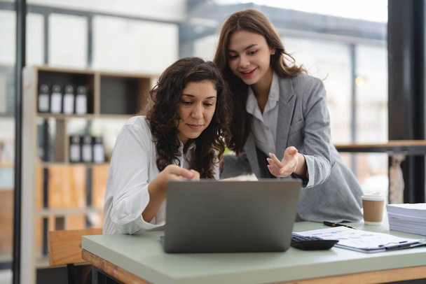 Dwoje inteligentnych, wielonarodowych biznesmenów współpracujących z laptopem podczas rozmowy o nowościach w pracy w biurze - Zdjęcie, obraz