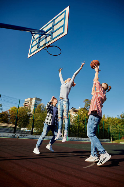Group of teens, students playing street basketball at basketball court outdoors at spring sunny day. Sport, leisure activities, hobbies, team, friendship. Boys and girl spending time together. - Φωτογραφία, εικόνα