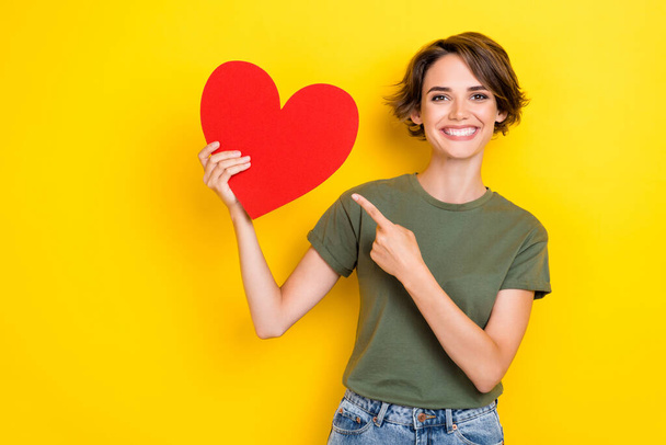 Photo of lovely toothy beaming woman bob hairdo dressed khaki t-shirt directing at big paper red like isolated on yellow color background. - Zdjęcie, obraz