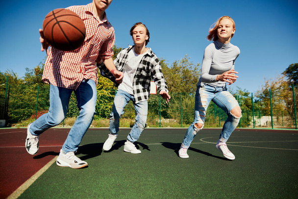 Group of teens, students playing street basketball at basketball court outdoors at spring sunny day. Sport, leisure activities, hobbies, team, friendship. Boys and girl spending time together. - Foto, afbeelding