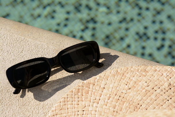 Stylish sunglasses near outdoor swimming pool on sunny day, closeup - Zdjęcie, obraz
