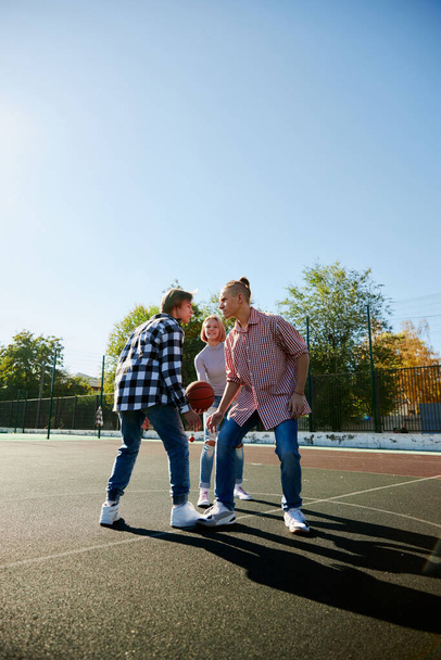 Leisure games. Group of friends bonding outdoors to play street basketball. Teens wearing casual style clothes. Look happy, delighted. Social gathering, friendship, team and happy childhood - Fotografie, Obrázek
