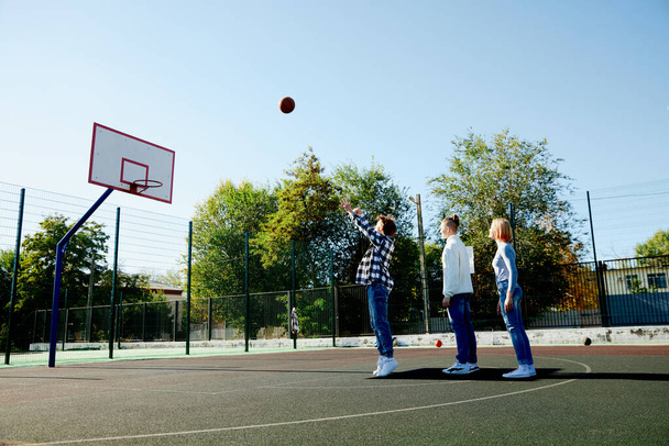 Group of teens, students playing street basketball at basketball court outdoors at spring sunny day. Sport, leisure activities, hobbies, team, friendship. Boys and girl spending time together. - Foto, Imagen
