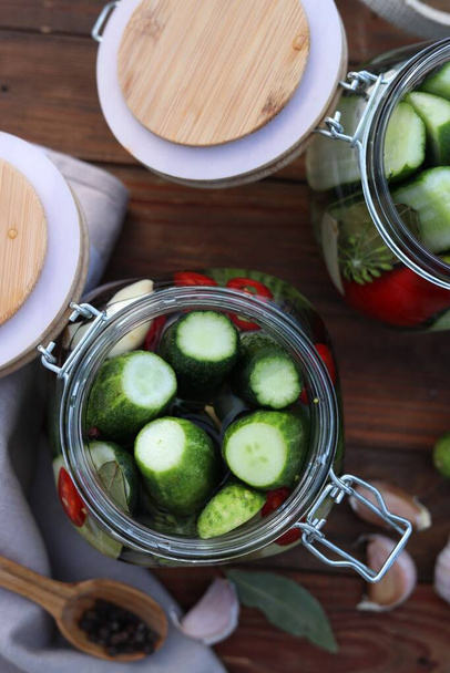 Glass jars with fresh cucumbers and other ingredients on wooden table, flat lay. Canning vegetables - Foto, afbeelding