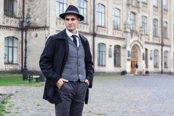 Men's photo shoot in a classic plaid suit and a hat against the backdrop of an old building. - Fotó, kép