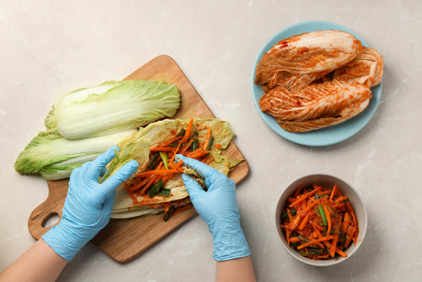 Woman preparing spicy cabbage kimchi at beige marble table, top view - Foto, Bild