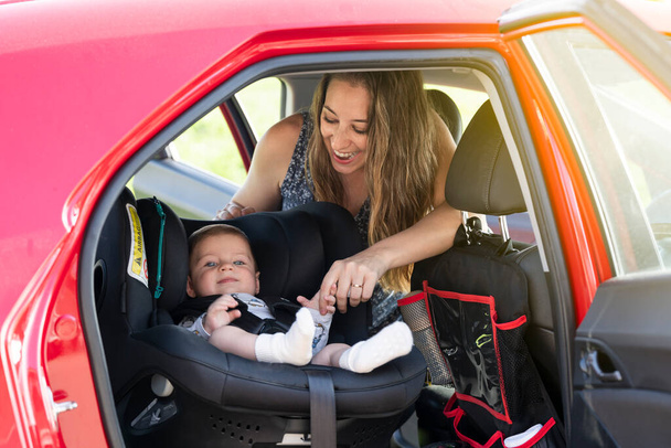 Junge Mutter setzt ihren kleinen Sohn in den Autositz und schnallt sich an - Foto, Bild