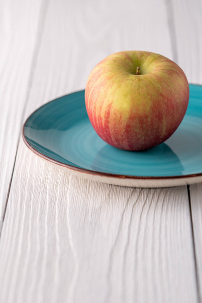 Piros zöld alma egy zöld kék tányéron egy fehér parasztház asztal - Fotó, kép