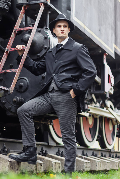 Männerfotosession im klassischen karierten Anzug und Hut vor der Kulisse einer alten Dampflok. - Foto, Bild