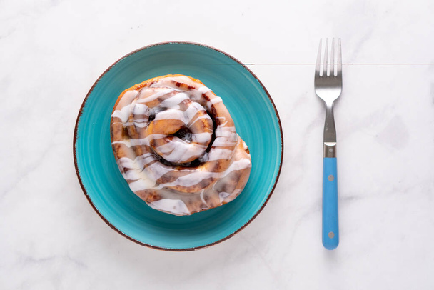 Large gourmet frosted cinnamon roll on marble table - Photo, Image