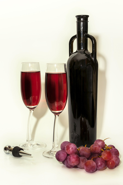 Botella de vino tinto original, uvas tintas y dos copas de vino en blanco
 - Foto, imagen