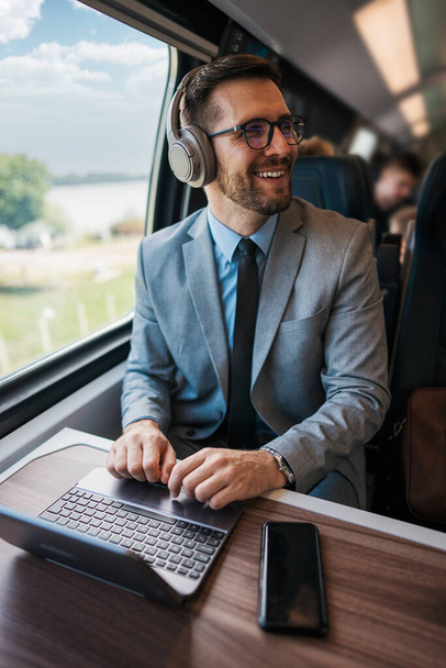 Handsome middle age businessman using his laptop computer while traveling with high-speed train. Modern and fast travel concept. - Foto, immagini