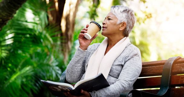 Ей всегда нравится читать свои книги в парке. пожилая женщина пьет кофе во время чтения книги в парке - Фото, изображение