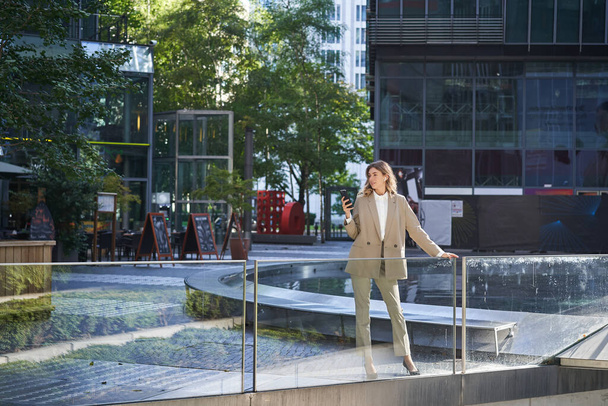 Впевнена бізнес-леді в бежевому костюмі, стоячи у позі влади в центрі міста
. - Фото, зображення