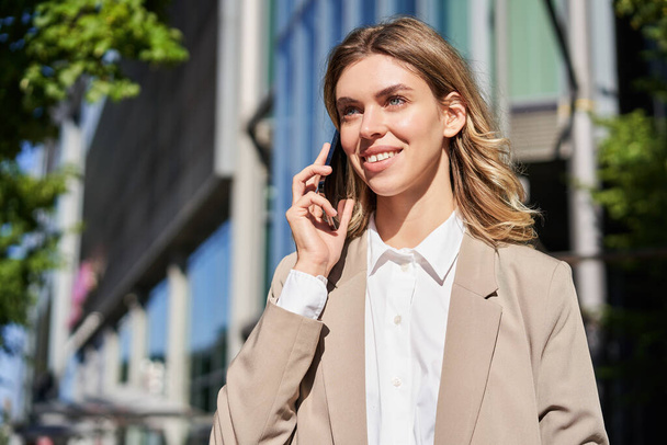 Portrait d'une femme d'affaires faisant un appel téléphonique, debout dans la rue près d'un immeuble de bureaux, parlant à quelqu'un au téléphone. - Photo, image