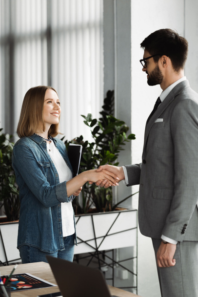 Smiling job seeker holding resume and shaking hand of businessman in office  - Photo, Image