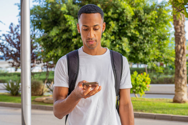 Side view of young african american man smiling happy using smartphone at street of city. - 写真・画像