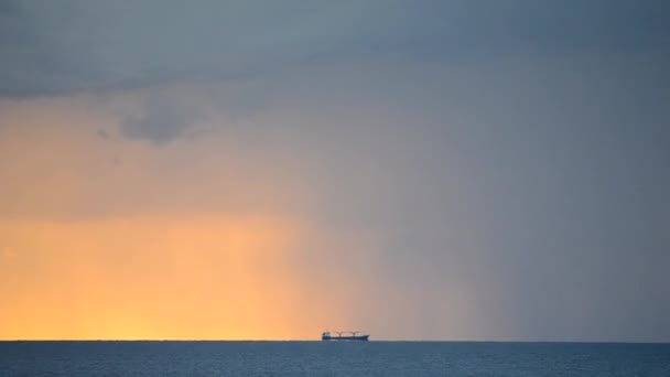 Bir tahıl taşıyıcı tanker, çok uzaklarda, deniz kenarında şafak vakti, yağmur ve büyük kara bulutlarla birlikte, arka planda kalır. Deniz manzarası, deniz manzarası. Doğal arka plan. Zaman Uygulaması - Video, Çekim