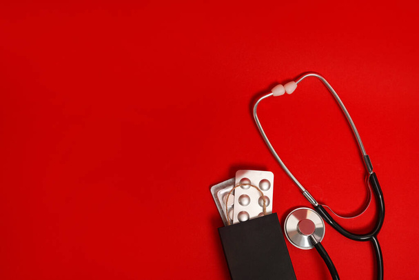 Stéthoscope avec pilules dans un sac en papier noir sur fond rouge, espace de copie, vendredi noir, médecine - Photo, image