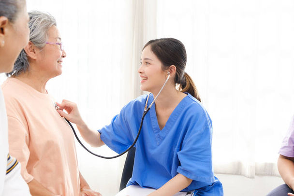 Aasialainen sairaanhoitaja, joka käyttää stetoskooppia vanhemman naispotilaan sykkeen tarkistamiseen kotona. Lääkintä. Hoitaja hoitokoti käsite. - Valokuva, kuva