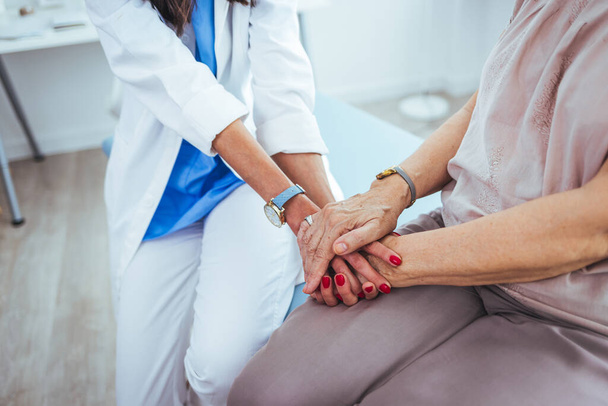 young female doctor holding hand of her senior patient in clinic - Foto, imagen