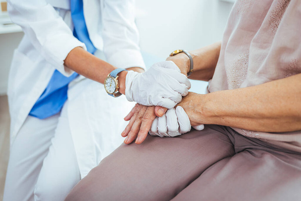 young female doctor holding hand of her senior patient in clinic - Zdjęcie, obraz
