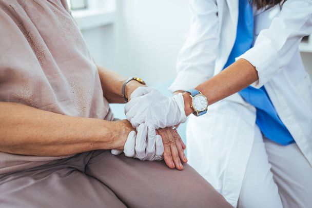 young female doctor holding hand of her senior patient in clinic - Foto, Bild