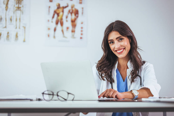 Portrait of female doctor seating in her office at clinic. Friendly Latin American female doctor at the hospital looking at the camera and smiling. Confident female doctor at office desk - Foto, imagen