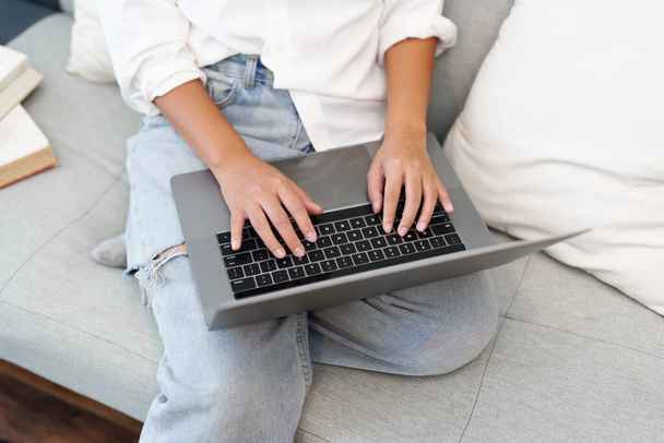 Portrait of a young Asian woman sitting on the sofa using a computer - 写真・画像