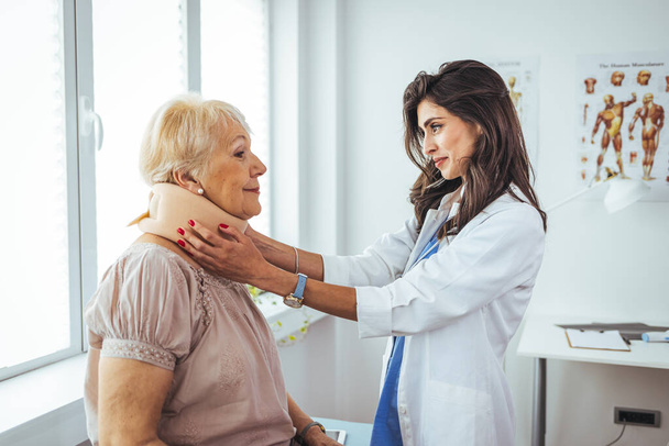 Portrait of a female doctor helping a senior woman at office with her neck injury a healthcare and medicine concepts. Doctor putting neck orthopaedic collar on adult injured woman  - Фото, зображення