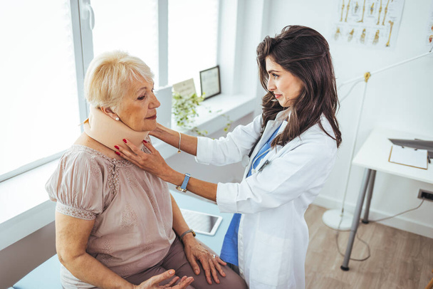 Young woman with injury of neck visiting doctor in clinic. Doctor examining a patient at desk in medical office. Doctor talking to a senior patient with cervical collar at the hospital - Foto, immagini