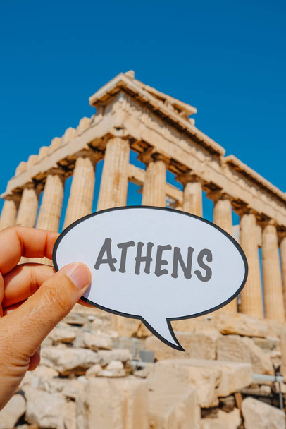 primo piano di un uomo che tiene un segno nella forma di una bolla di discorso con la parola Atene scritta in esso, davanti al Partenone, nell'Acropoli di Atene, Grecia, in un giorno d'estate - Foto, immagini