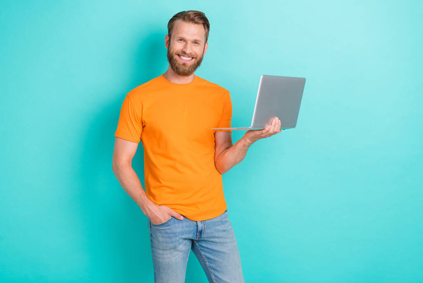 Portrait of positive satisfied man toothy smile hold wireless netbook isolated on aquamarine color background. - 写真・画像
