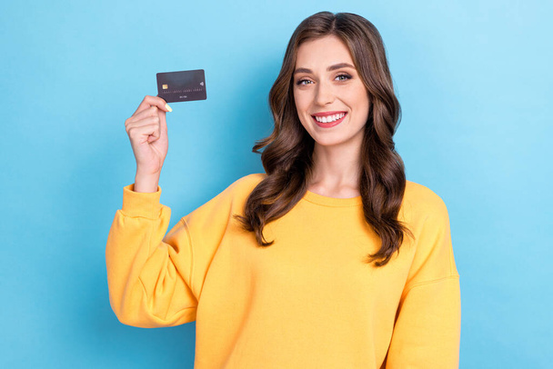 Photo of young attractive pretty gorgeous woman wear yellow swetshirt hold credit card toothy smile beaming recommend bank isolated on blue color background. - Fotoğraf, Görsel