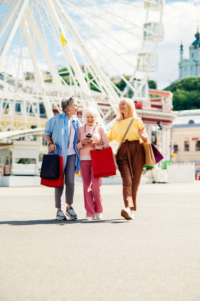Счастливые пожилые женщины, встречающиеся на свежем воздухе и совершающие покупки в центре города - Прекрасные и веселые пожилые женщины объединяются и веселятся на свежем воздухе - Фото, изображение