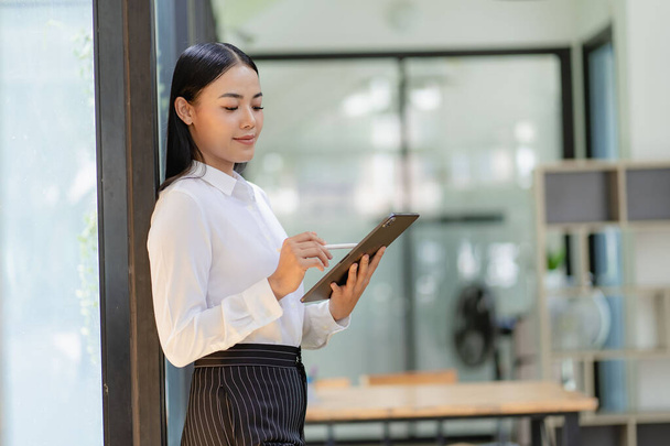 Happy Asian female salesperson looking at camera Smiling female executive manager offering professional business services holding digital tablet standing in office - Photo, Image